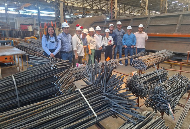 Foto mostra um grupo de pessoas posando para fotografia, tendo como plano principal um montante de ferragens