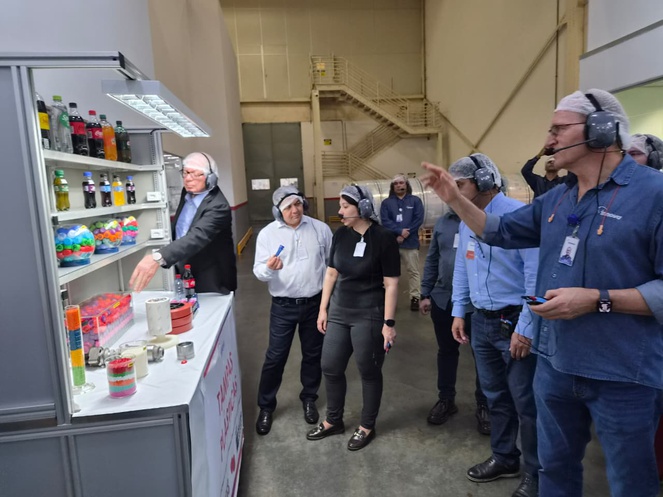 Foto mostra pessoas olhando para produtos plásticos dentro de uma empresa