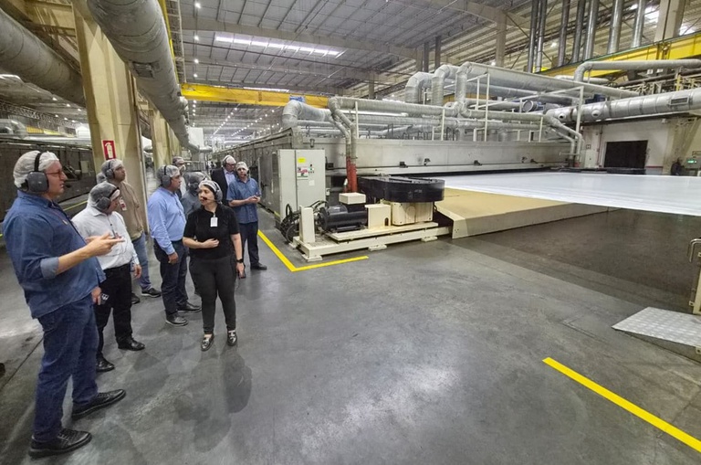 Foto mostra pessoas olhando para uma máquina de fabricar produtos plásticos