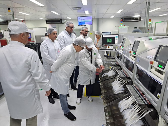 Foto mostra homem de boné e jaleco brancos mostrando equipamentos a grupo de pessoas vestidas de jaleco e touca brancos