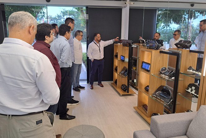 Foto mostra homem de blusa branca e barba apresentando acessórios de automóveis para grupo de pessoas