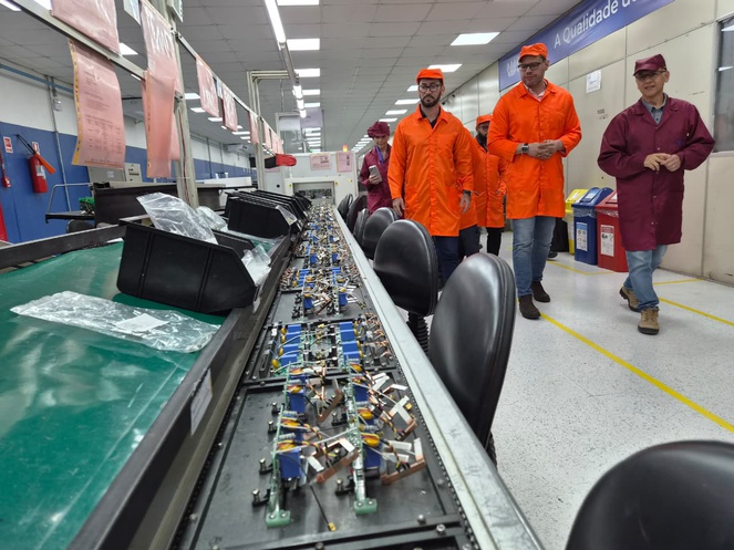 Foto mostra homens visitando linha de produção de medidores de energia