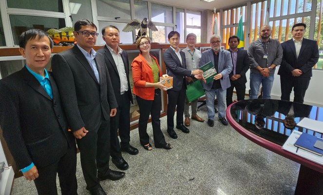 Foto mostra homens segurando um livro, ao lado de outros homens, durante uma cessão para foto, realizada após reunião lanando durante reunião com outros homens em uma sala fechada