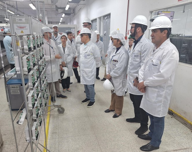 Foto mostra homem de boné branco conversando com grupo de pessoas vestidas com jaleco branco e usando capacete branco
