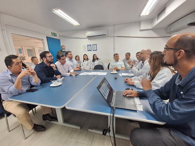 Foto mostra homem de óculos e careca falando, com outras pessoas observando, durante uma reunião