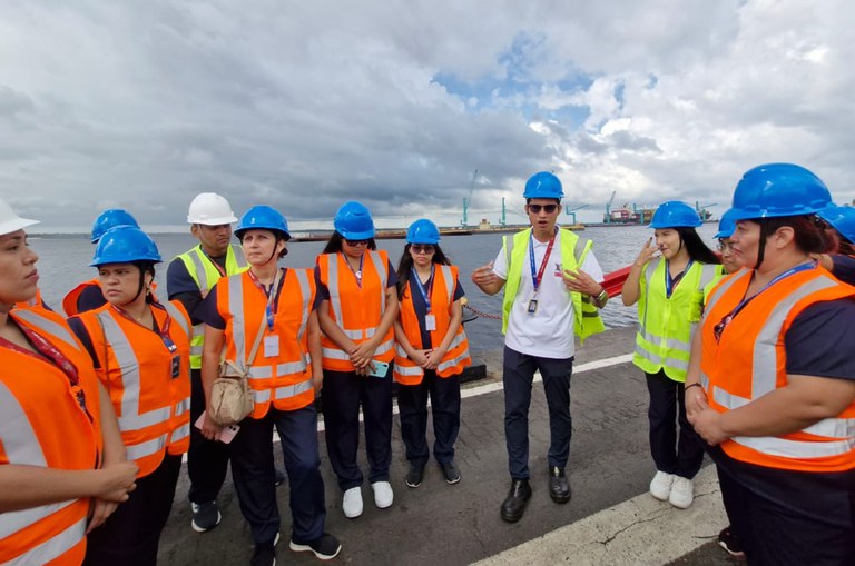 Foto mostra pessoas com capacete e colete, durante visita a um porto flutuante
