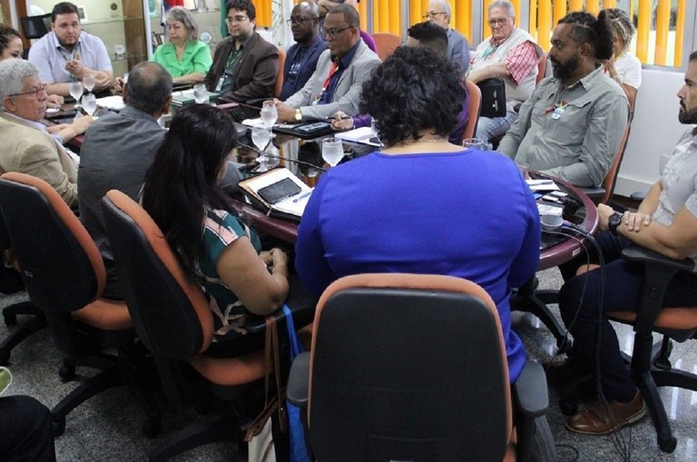 Foto mostra grupos de pessoas numa reunião institucional em sala fechada