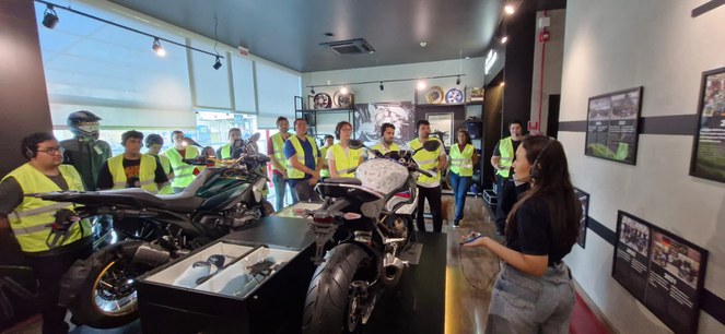 Foto mostra mulher com aparelho na mão e fone de ouvido dando uma explicação a um grupo de pessoas