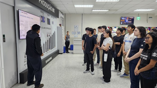 Foto mostra homem homem mostrando um painel de informações a um grupo de estudantes