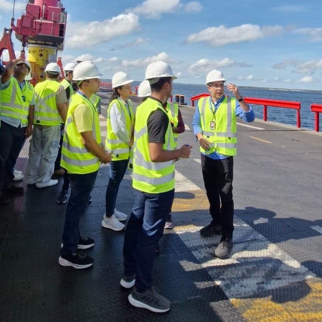 Foto mostra um grupo de pessoas vestidas de jaleco verde em visita a um porto flutuante