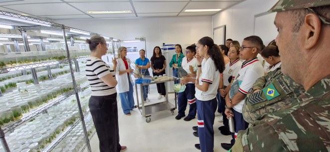 Foto mostra mulher de blusa listrada fazendo uma explicação a um grupo de estudantes