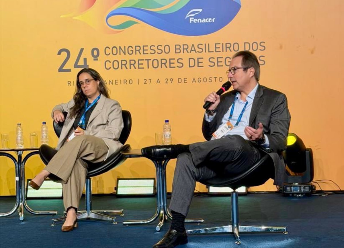 Diretora Júlia Lins à esquerda e Diretor Marcilio Nascimento à direita. Painel amarelo do 24º Congresso Brasileiro dos Corretores de Seguros ao fundo.
