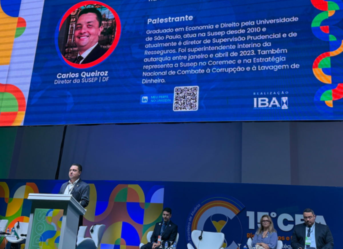 Foto do Diretor Carlos Queiroz no palco do evento com o currículo resumido dele no telão ao fundo