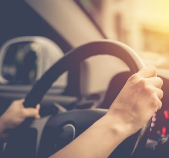 Pessoa com as mão no volante dirigindo um carro.