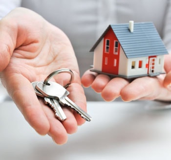 Pessoa mostrando em uma das mãos um molhe de chaves e na outra uma casa em miniatura.
