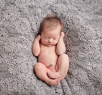 Bebê recém nascido deitado sobre uma manta cinza.