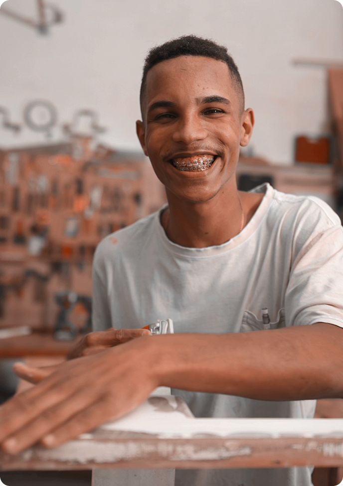 Homem de pele escura, com uma camisa de coloração cinza, sorrindo.