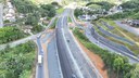 Imagem aérea de uma rodovia em obras, cercada por áreas verdes e residências, com tráfego fluindo.