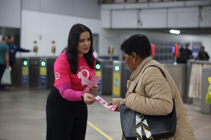 Voluntária do Instituto da Mama distribui material informativo a uma usuária no saguão de entrada da Estação Mercado da Trensurb, durante ação de conscientização..