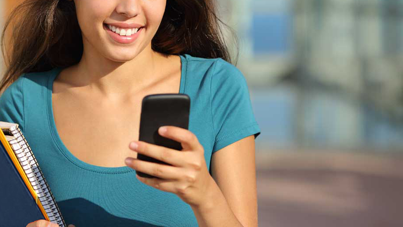 Uma estudante olha sorridente a tela de um celular