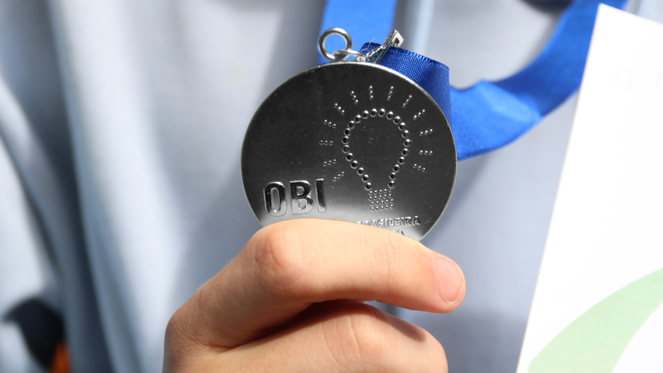 Mão segurando uma medalha de prata da OBI