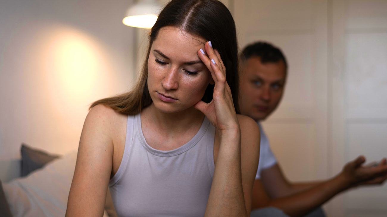 Imagem de uma mulher triste e um homem ao fundo gesticulando