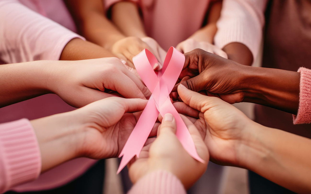 mãos feminias seguram o laço que simboliza a Campanha Outubro Rosa