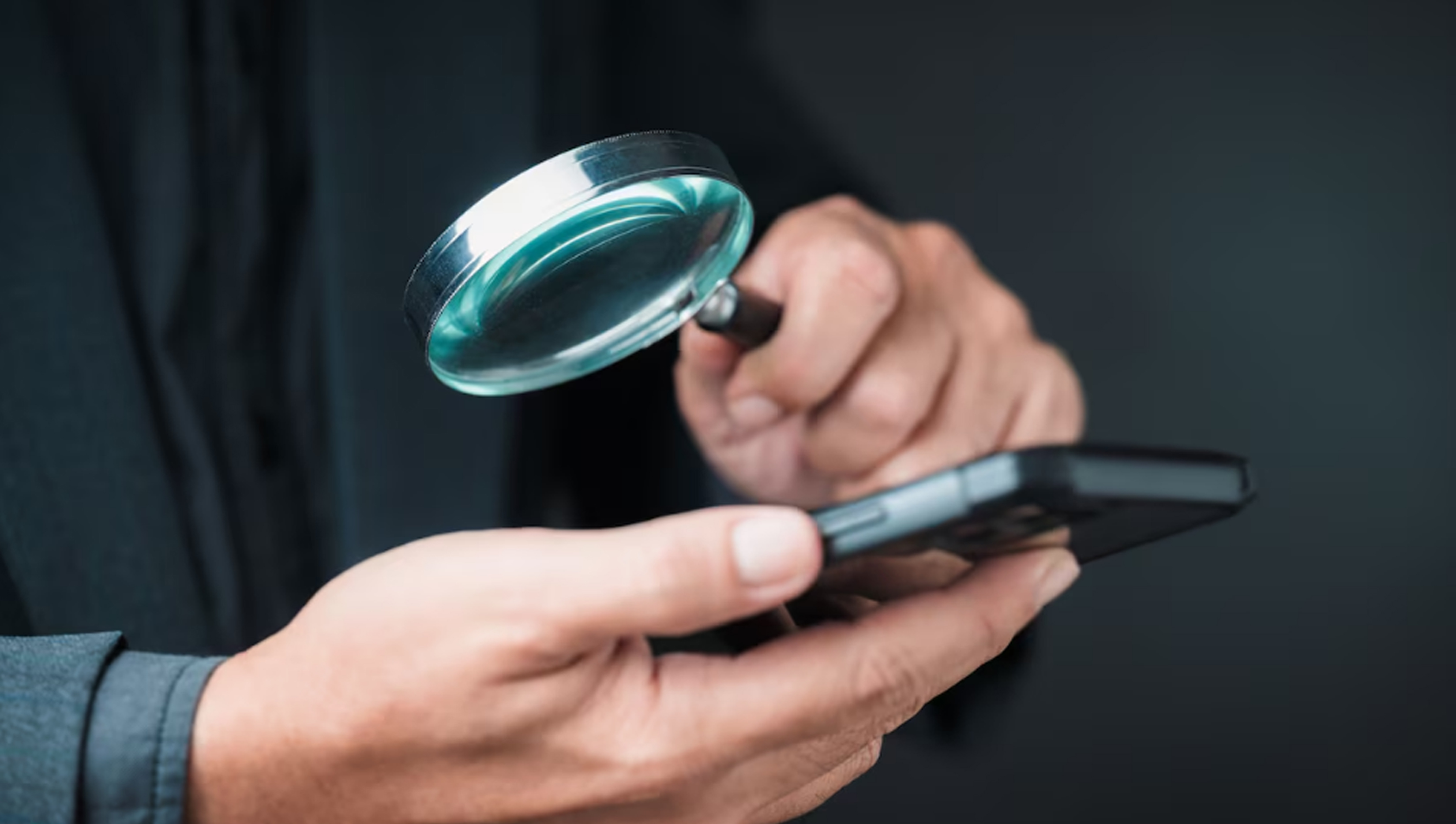 mãos segurando uma lupa e um celular simulando checagem