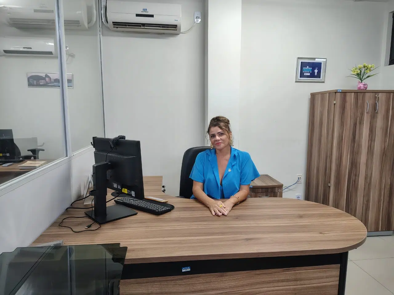 mulher vestindo blusa azul sentada á mesa ao lado de um computador