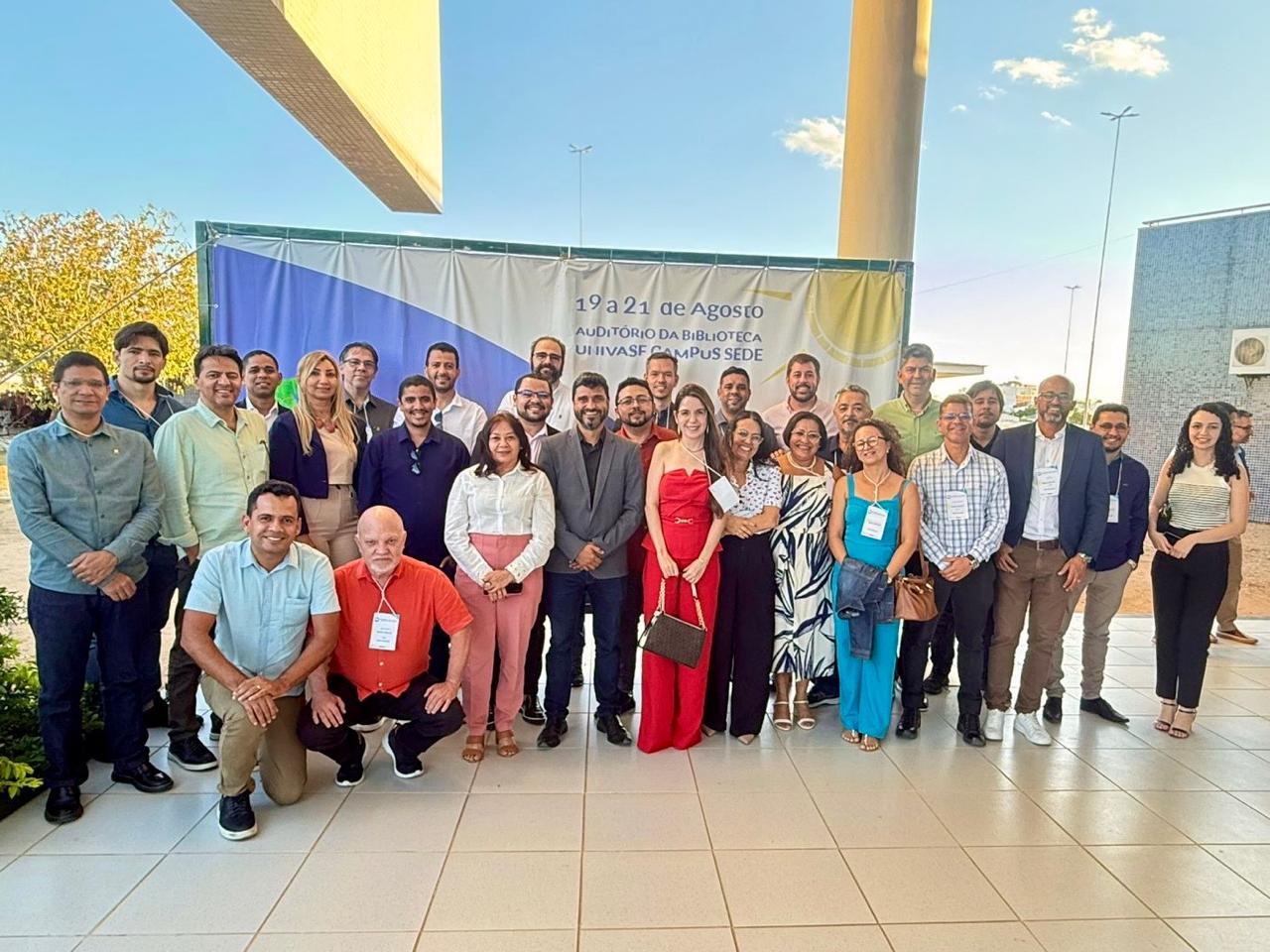Fotografia em grupo dos participantes da reunião da SEPLAN posando em ambiente externo, em frente a um banner do evento realizado na UNIVASF.